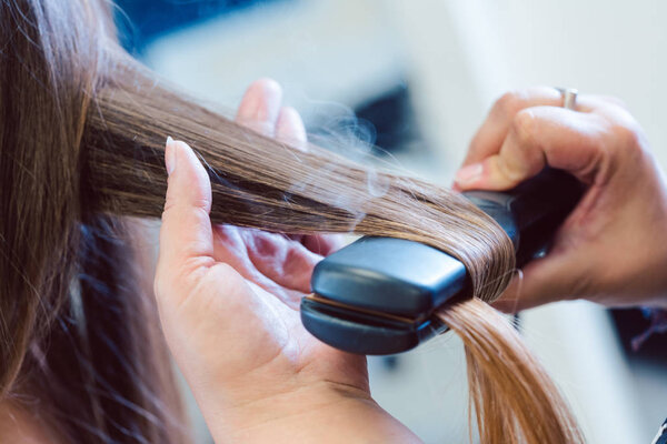 Hairdresser using flat iron on hair of woman customer