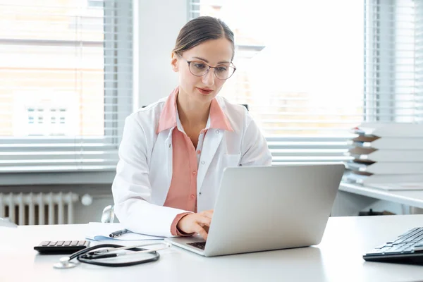 Médico fazendo papelada no computador sentado na mesa — Fotografia de Stock