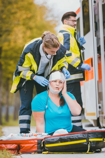 Akut sjukvårdare dressing huvud såret av skadade kvinnan — Stockfoto