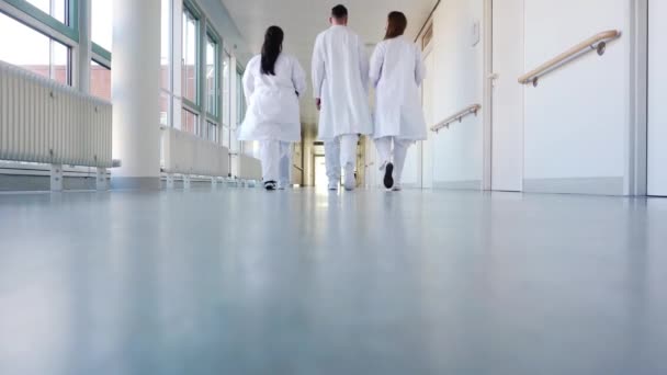 Tres doctores caminando por un pasillo en el hospital — Vídeo de stock