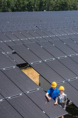 Bir elektrik santralinde güneş pillerinin arasında duran iki kişi