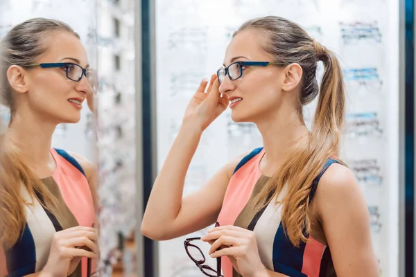 Mujer joven en la tienda de optometristas revisando sus miradas en el espejo —  Fotos de Stock