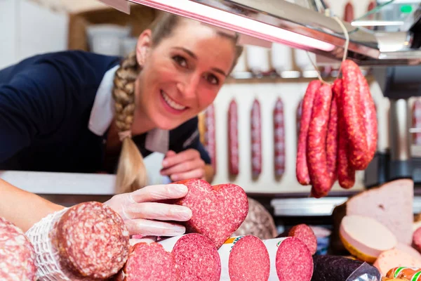 Vendas mulher na loja de carne mostrando uma salsicha em forma de coração — Fotografia de Stock