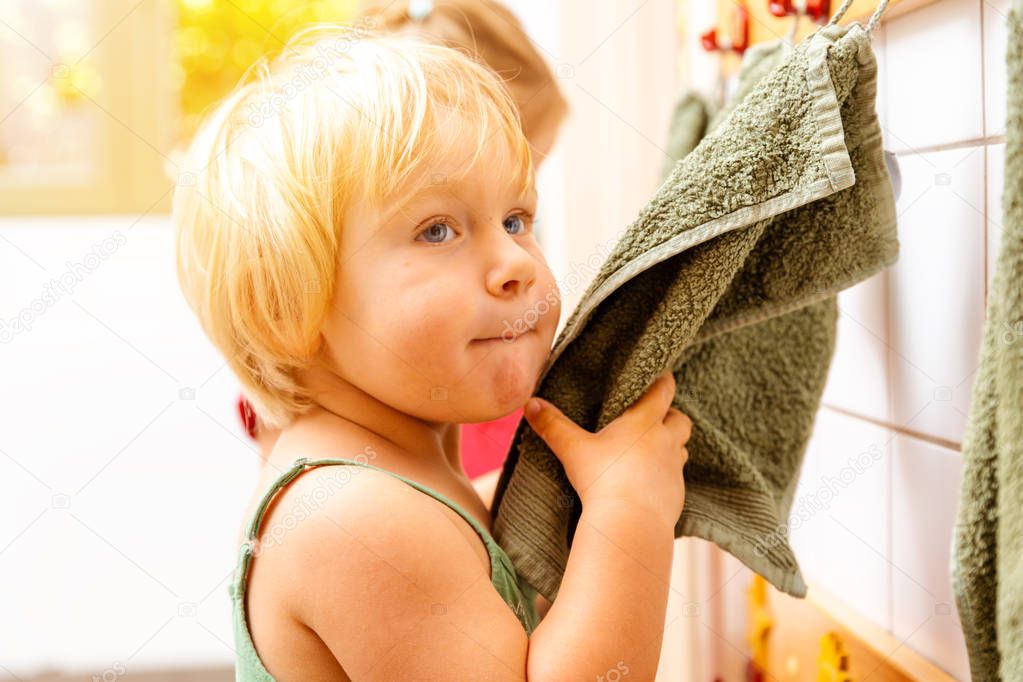 Little girl in nursery school using towel in bathroom