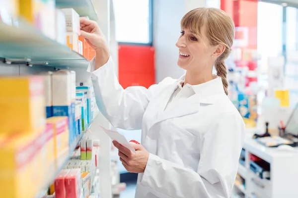 Farmacêutico ou Químico mulher classificando medicamentos em prateleiras em sua farmácia — Fotografia de Stock