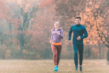 Harika sonbahar manzarası olan bir çift daha iyi spor yapmak için koşuyor.