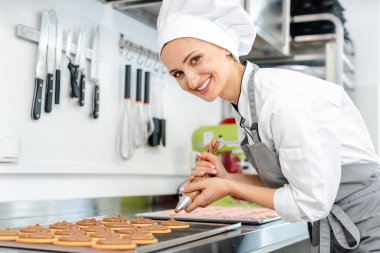 Şekerci kadın kurabiyelerin üstüne krema koymak için pasta torbası kullanıyor.