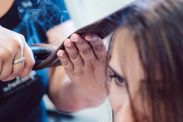Hairdresser using flat iron on hair of woman customer — Stock Photo, Image