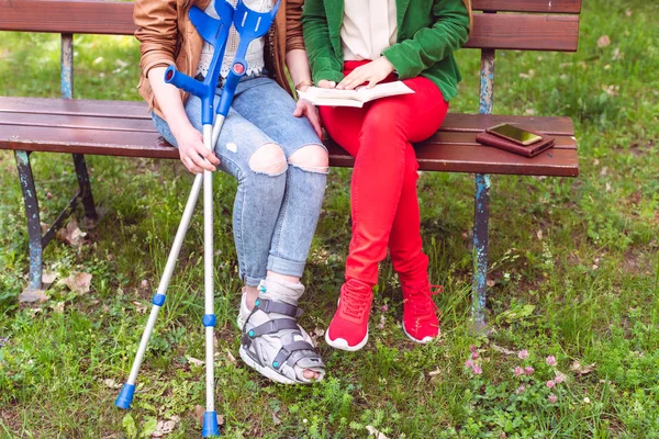 Dois amigos lendo um livro no parque, um tem um pé quebrado — Fotografia de Stock