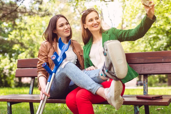 Meilleurs amis avec un ayant une jambe cassée prenant un selfie — Photo