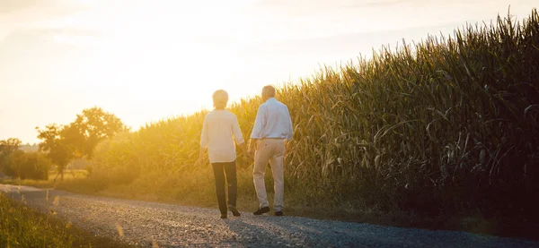 Donna anziana e uomo che passeggiano lungo un campo — Foto Stock