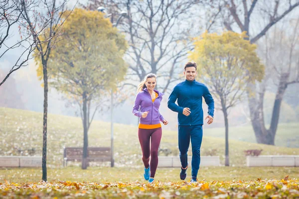 Woman and man running in autumn park for sport — Stock Photo, Image
