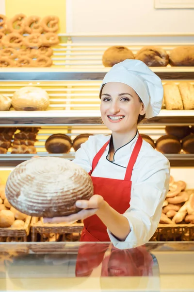 Vendedora con delantal presentando pan fresco en una panadería — Foto de Stock