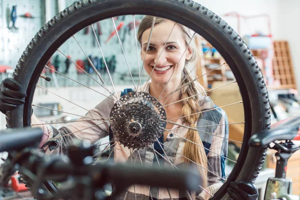 Fiets monteur vrouw kijken door het wiel van de fiets — Stockfoto