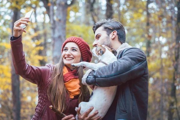 Wanita dan pria dengan anjing mereka di musim gugur berjalan mengambil selfie telepon — Stok Foto
