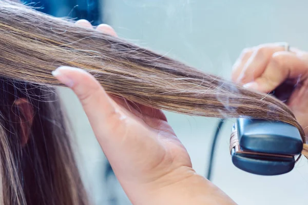 Hairdresser using flat iron on hair of woman customer — Stock Photo, Image