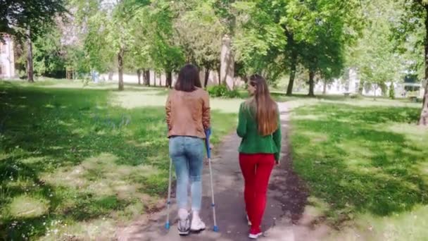 Femme en bonne santé et ami avec la jambe cassée ayant une promenade ensemble — Video