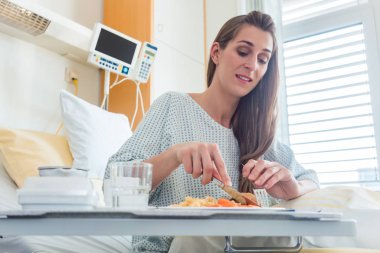 Patient in hospital lying in bed eating meal clipart