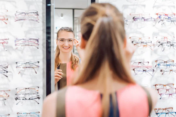 Young woman trying fashionable glasses in optometrist store
