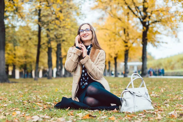 Frau sitzt im Herbst mit Handy im Gras — Stockfoto