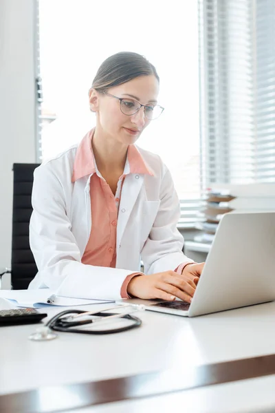 Médico fazendo papelada no computador sentado na mesa — Fotografia de Stock