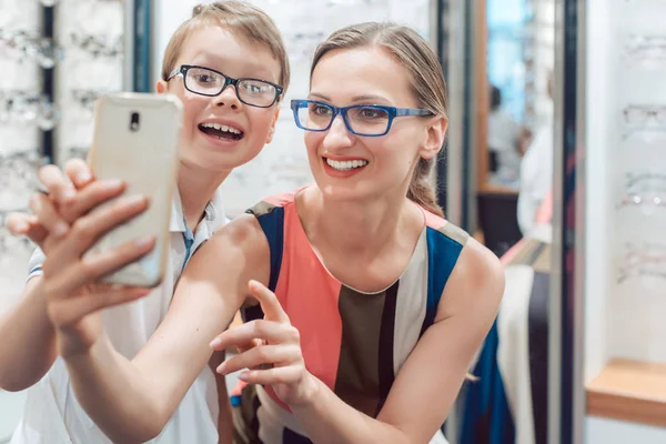 Mor och son tar selfie med nya glasögon på optiker shop — Stockfoto