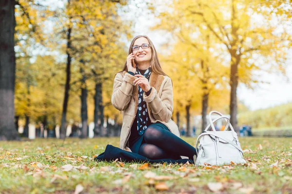 Frau sitzt im Herbst mit Handy im Gras — Stockfoto