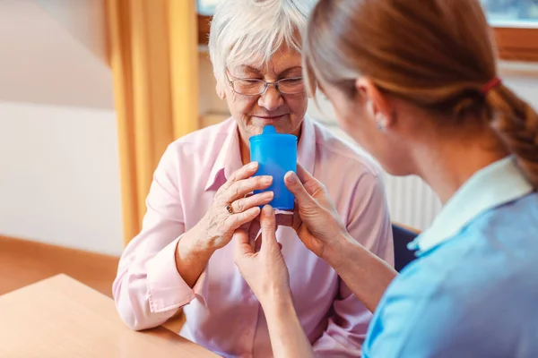 Caregiver helping senior woman drinking giving her a cup of water — Stock Photo, Image