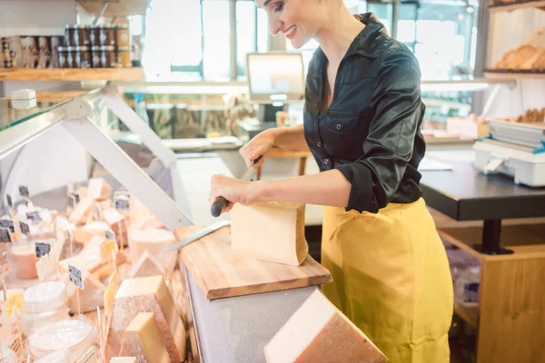 Joven empleado de tienda en delicatessen cortar queso —  Fotos de Stock