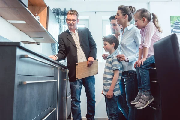 Vendedor mostrando à família as características de uma nova cozinha — Fotografia de Stock