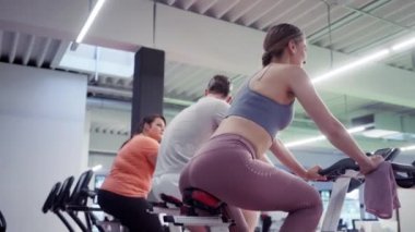 Erkekler ve kadınlar spor salonunda spor bisikletleriyle dönüyorlar.