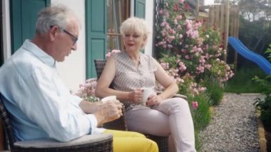 Üst düzey çift evlerinin önündeki verandada kahvelerini yudumluyorlar.