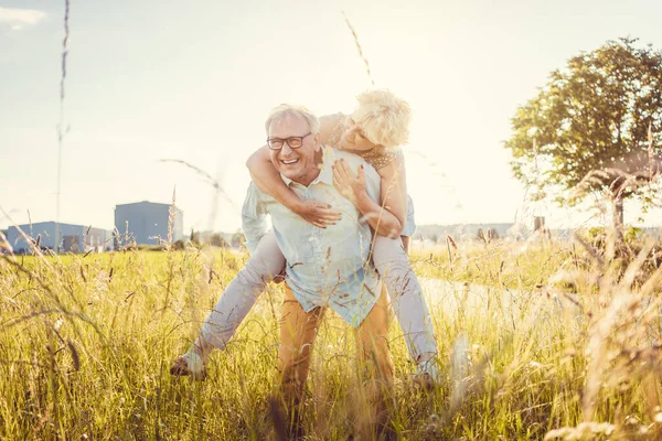 Strong senior man carrying his wife piggyback without back pain — Stock Photo, Image