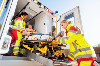 Sağlık görevlileri yaralı adamı ambulansla sedyeye koyuyor.