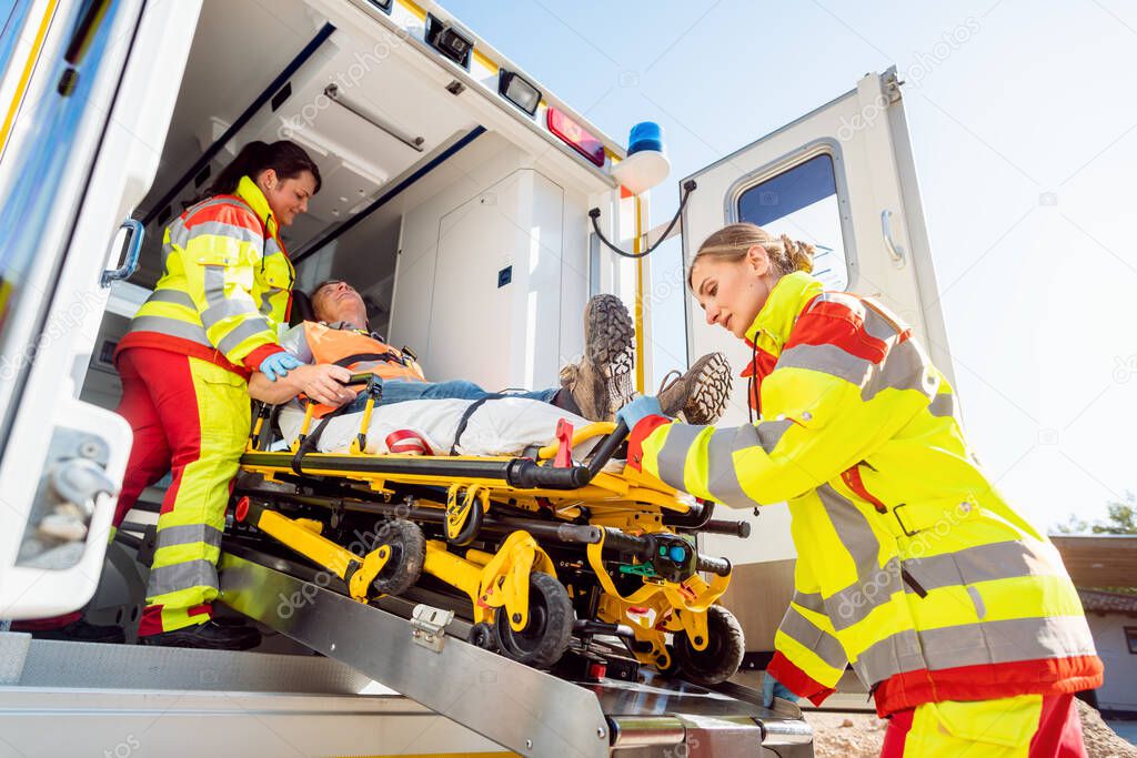 Paramedics putting injured man on stretcher in ambulance car