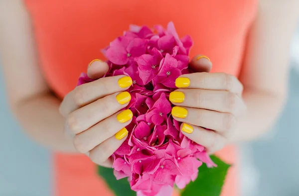 Women with manicured nails in yellow holding a flower — Stock Photo, Image