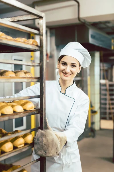 Baker vrouw duwen lakens met brood in de bakoven — Stockfoto