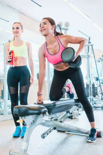 Kraftfull ung kvinna ler samtidigt rodd med en arm i en trendig gym — Stockfoto