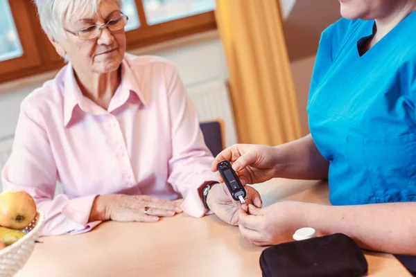 Infermiera amministra il test del diabete per anziani in casa di cura — Foto Stock