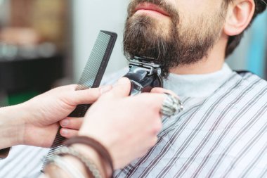 Berber müşterinin sakalını kesiyor.