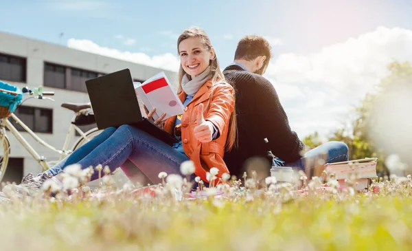 Studentin sitzt mit erhobenem Daumen im Gras vor Universitätsgebäude — Stockfoto