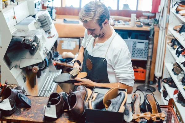 Shoemaker with shoes to repair on a rack in his workshop — Stock Photo, Image