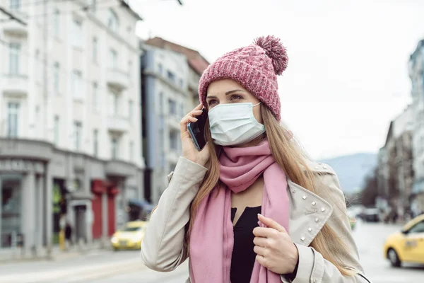 Mujer preocupada usando su teléfono usando máscara médica y guantes — Foto de Stock