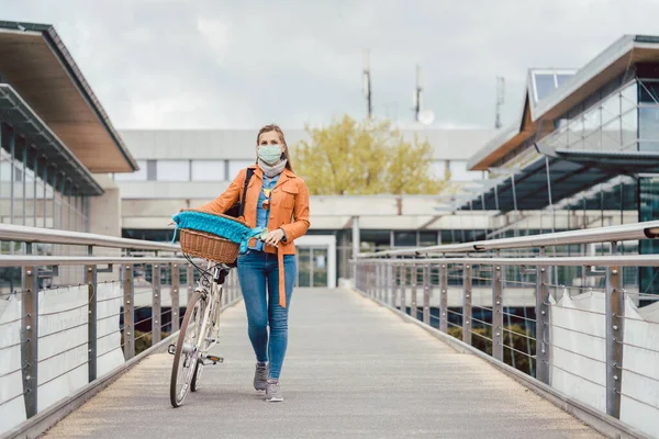 Mulher com máscara facial empurrando sua bicicleta sobre uma ponte — Fotografia de Stock