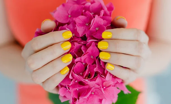 Женщины с ухоженными ногтями в желтом с цветком в руках — стоковое фото