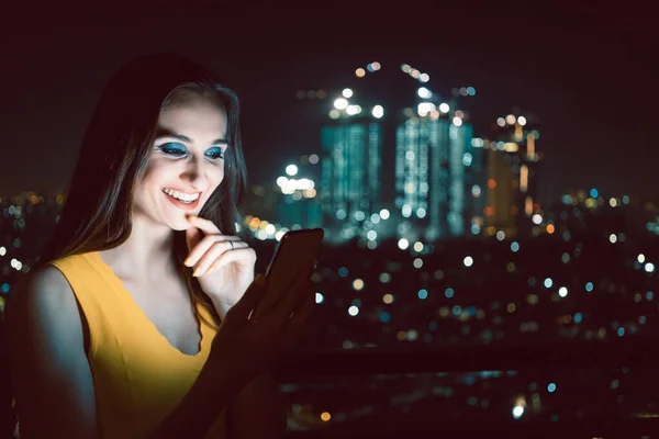 Şehir siluetinin önünde telefonunu kontrol eden kadın. — Stok fotoğraf