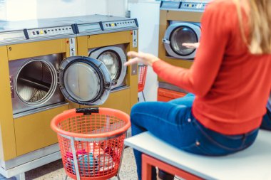 Çamaşırhanedeki kadın çamaşır makinesinin önünde şaşkın şaşkın oturuyor.