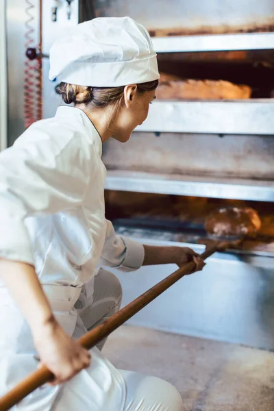 Panadero poniendo pan en el horno de panadería — Foto de Stock