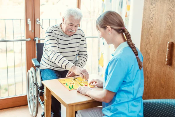 Νοσοκόμα και τελειόφοιτος στο γηροκομείο παίζουν επιτραπέζιο παιχνίδι — Φωτογραφία Αρχείου