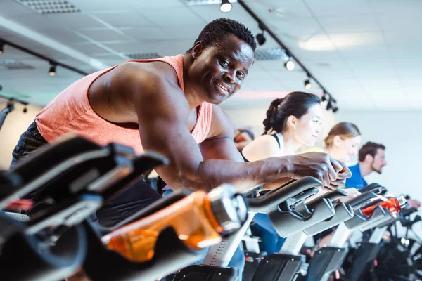 Hombre africano y amigos en bicicleta de fitness en el gimnasio — Foto de Stock